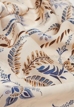 Krämfärgad tyg med intrikata blå och bruna botaniska mönster, med flödande veck och en mjuk, silkig textur.