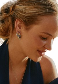 Silver earrings shaped like interlocking hearts, featuring a polished finish and hanging hooks, worn by a person with a side profile.