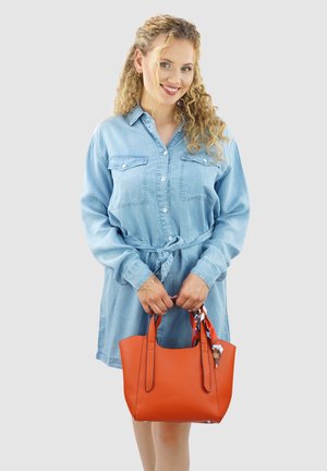 Oranje leren tote bag met twee stevige handvatten, voorzien van een decoratieve sjaal die aan het handvat is geknoopt. Gladde textuur, gestructureerde vorm.
