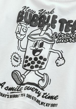 Černý grafický obrázek usmívajícího se kelímku bubble tea s velkými tapiokovými perličkami, držícího krabici mléka, na bílém tričku. Text obsahuje "New York BUBBLE TEA."