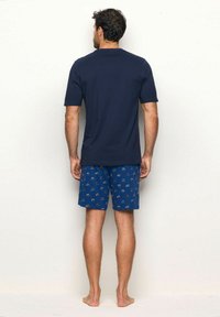 Cămașă pentru bărbați cu mânecă scurtă de culoare bleumarin, asociată cu pantaloni scurți albaștri cu un model ce include mici desene. Fabricat din bumbac, cu o croială lejeră și fără elemente hardware vizibile.