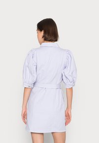 Vestido lilás claro com mangas bufantes, colarinho e cinto na cintura; apresenta uma saia reta e punhos abotoados; textura de tecido suave.