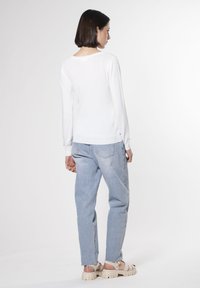 Top bianco a maniche lunghe con scollatura rotonda, abbinato a jeans dritti blu chiaro e sandali beige a zeppa. Tessuto liscio, design semplice.