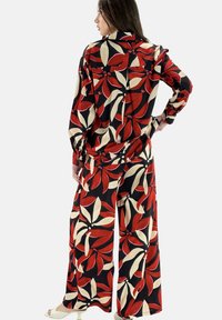 Ensemble floral deux pièces avec un fond noir et des motifs de feuilles rouges et crème. Haut ample à manches longues et pantalon large.