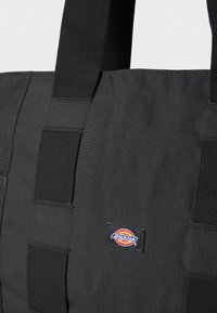 Svart totebag laget av slitesterkt stoff med tykke stropper. Har et sydd merke med merket "Dickies" i rød, gul og blå farge.