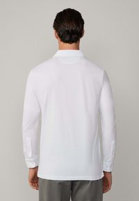 Weißes langärmliges Polohemd mit klassischem Kragen, geknöpften Manschetten und glatter Textur. Sauberes, einfaches Design ohne Muster.