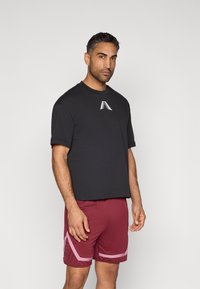 Čierne bavlnené tričko s krátkymi rukávmi a okrúhlym výstrihom, s bielym logom. Spárované s bordovými šortkami s ružovými akcentmi.