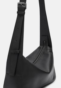 Zwarte leren schoudertas met een gestructureerde vorm, verstelbare schouderband en een opvallende ritssluiting langs één kant. Glad textuur.