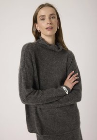 Maglione grigio a maglia con collo a cowl, maniche lunghe e vestibilità ampia. Tessuto morbido, motivo sottile, abbinato a un bracciale in argento.