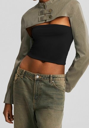 Kort olijfgroen jack met gespdetails gecombineerd met een zwarte tube top en een hoog getailleerde vervaagde olijfgroene jeans op het model.