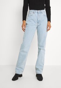 Jeans in denim azzurro chiaro con vestibilità rilassata, vita alta, cinque tasche e cuciture a contrasto. Indossati con un top nero a coste a maniche lunghe.