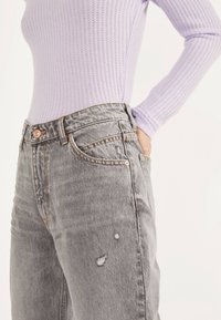 Jeans de mezclilla gris con un patrón desgastado, que cuentan con herrajes de cobre y una cintura alta; combinados con una blusa de manga larga acanalada de color lila claro.