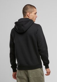 Felpa nera con cappuccio e casco, dal taglio rilassato. Tessuto morbido, polsini e orlo a costine. Il modello indossa pantaloni verde chiaro.