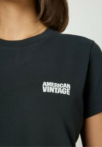 Must ehk musta puuvillane T-särk, millel on sooniline ümar kaelus ja valge "AMERICAN VINTAGE" logo vasakul rinnal. Lühikesed varrukad, ühtlane tekstuur.