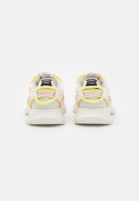 Sportovní obuv s bílým síťovaným svrškem, doplněná žlutými a meruňkovými detaily, s robustní podrážkou a zadním poutkem pro snadné obouvání.