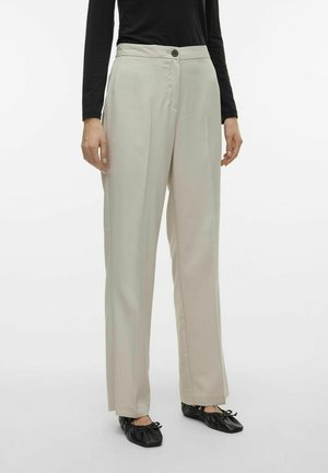 Pantalones beige de corte ajustado con una cintura alta, bolsillos delanteros y cierre de un solo botón. Se llevan con zapatos planos negros.