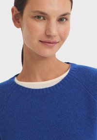 Blue knitted sweater with a round neckline and raglan sleeves, featuring textured fabric and a ribbed collar.