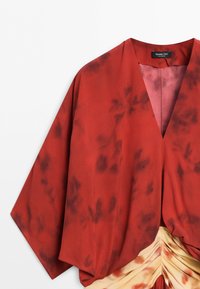 Red kimono-style top with wide sleeves and subtle darker floral patterns, paired with cream fabric featuring soft red tie-dye and pleats.