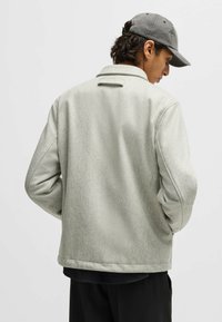 Light gray wool-blend jacket with a textured finish, classic collar, and slightly oversized fit. Paired with a gray cap.