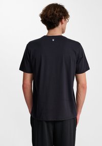 Czarny bawełniany t-shirt z krótkim rękawem, okrągłym dekoltem oraz małym białym logo blisko tylnego dekoltu. Gładka tekstura.