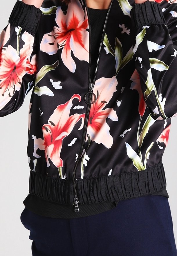 Veste bomber noire avec grand imprimé floral rose et blanc, poignets et ourlet côtelés, et fermeture éclair frontale. Texture de tissu lisse et brillant.
