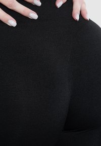 Zwarte leggings gemaakt van een gladde, rekbare stof. Close-up weergave die de textuur van het materiaal en het aansluitende ontwerp benadrukt, met de nadruk op het gebied van de tailleband.
