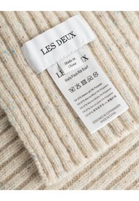 Krämfärgad ribbad scarf med färgklickar. Etiketten läser "LES DEUX" och innehåller skötselinstruktioner. Tillverkad av 97% merinoull och 3% polyester.