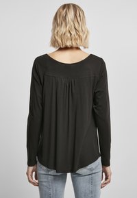 Zwarte longsleeve shirt, zachte stof, ronde halslijn, geplooid achterdetail, gebogen zoom. Draagt met lichtblauwe jeans.