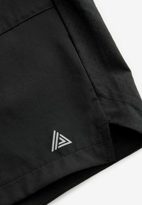 Sorte sporty shorts med en glat tekstur, der har perforerede paneler og et reflekterende trekantet logo nederst til venstre.