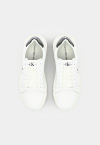 Fehér bőrsneaker kerek orral, fűzős kialakítással, fekete belső béléssel és emboszált logóval. Simaság és minimalista esztétika jellemzi.
