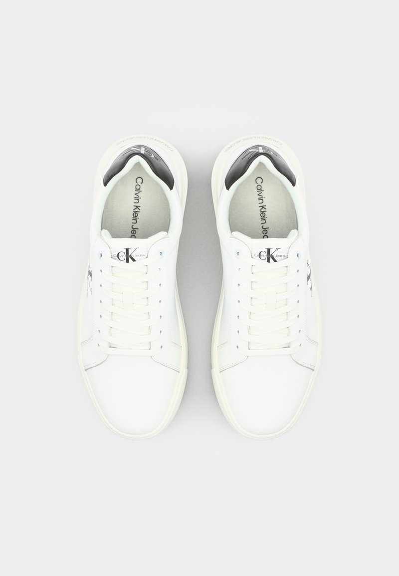 Baskets en cuir blanc avec bout arrondi, design à lacets, doublure intérieure noire et logo en relief. Texture lisse et esthétique minimaliste.