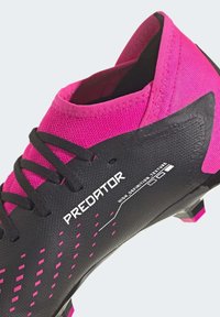 Mustat ja vaaleanpunaiset jalkapallokengät, joissa on teksturoitu pinta, mustat nauhat, pehmustettu nilkkaremmi ja vaaleanpunaisia yksityiskohtia pohjassa.