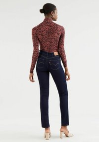 Röd blommig långärmad topp i kombination med mörkblå skinny jeans. Jeansen har en läderetikett, två bakfickor och kontrasterande söm.