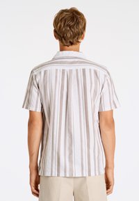 Camicia a maniche corte realizzata in tessuto leggero, con righe verticali marroni chiare e bianche, colletto con bottoni e retro semplice.