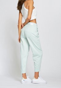 Mentolově zelené kalhoty s vysokým pasem a volným střihem, s kapsami vzadu a štítkem na pásku. Spárované s bílými sportovními botami.