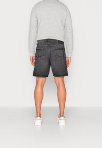 Pantalones cortos de mezclilla negra con un corte recto, que cuentan con dos bolsillos traseros y un dobladillo sin rematar. Se combinan con un sudadera gris claro y zapatillas blancas.