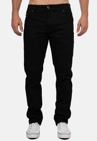 Jeans in denim nero con taglio dritto, design a cinque tasche e chiusura con bottone in metallo, abbinati a sneakers bianche.