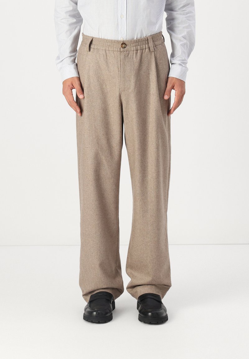 Beige, Wollmischung-Hosen im geraden Schnitt mit einem einzelnen Knopfverschluss und seitlichen Taschen, kombiniert mit schwarzen Slippers.
