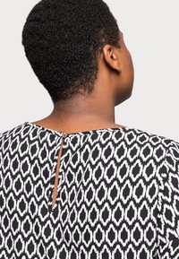 Schwarz-weiße gemusterte Bluse mit einem Schlüsselloch-Detail im Rücken, rundem Ausschnitt und kurzen Ärmeln; aus leichtem, strukturiertem Stoff gefertigt.