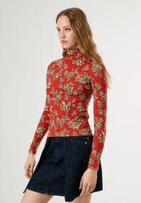 Crvena duga rukava turtleneck majica s cvjetnim uzorkom u boji vrhnja. Uparena s tamnoplavom traper suknjom. Glatka tkanina s prilagođenim siluetom.