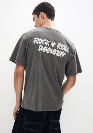 Grå bomulds t-shirt med korte ærmer og løs pasform, med hvid "ROCK N' ROLL DAMNATION" tekst på ryggen.