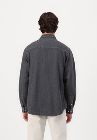 Herren Hemd in Dunkelgrau mit Knöpfen, langen Ärmeln, einer Brusttasche auf der linken Seite und geradem Saum. Leichter Stoff mit leichter Textur.