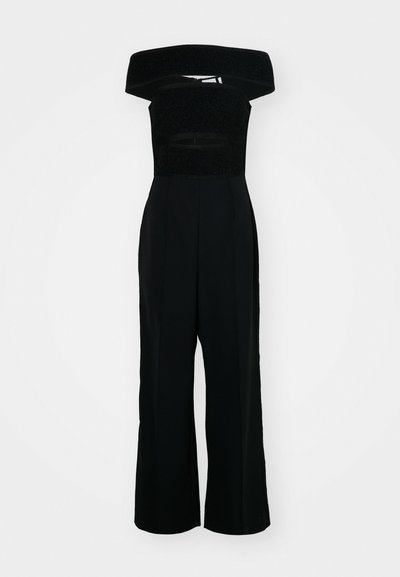 Salopetă neagră cu un design fără umeri, având un corp texturat și o siluetă cu picioare largi. Material neted cu detalii minime.
