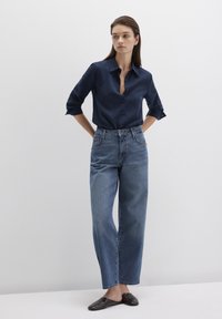 Navy button-up shirt with rolled sleeves, paired with high-waisted, wide-leg light blue denim jeans and black slip-on shoes.