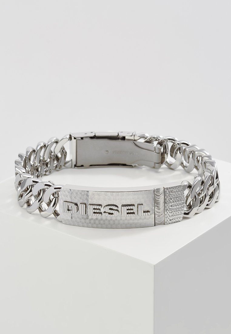Bracelet en chaîne argentée avec un bandeau texturé portant l'inscription "DIESEL", des maillons lisses et une fermeture à clapet. Les accents incluent des motifs de surface variés.