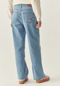 Jeans a gamba larga di un azzurro chiaro con design floreale ricamato sulle tasche posteriori, caratterizzati da una classica trama in denim e una vestibilità rilassata.