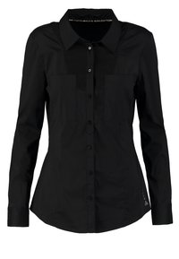 Czarna koszula z długim rękawem wykonana z gładkiego materiału; ma wyrazisty kołnierzyk, dwie kieszenie na piersi oraz dopasowany krój.