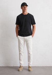 Schwarzes Baumwoll-T-Shirt, weiße Baumwollhosen, beige Schuhe. Einfaches Design, kurze Ärmel und eine taillierte Silhouette. Schirmmütze fügt Detail hinzu.