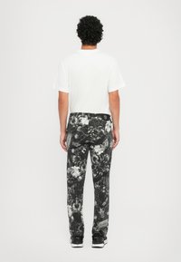 Pantalones de patrón en blanco y negro con diseños florales y abstractos, combinados con una camiseta blanca lisa, vistos desde atrás.