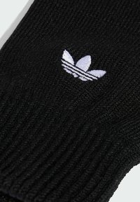 Mustast kudumist kinnas, millel on sooniktekstuur ja väike valge broderi Adidasi trefoil logo randme piirkonnas.